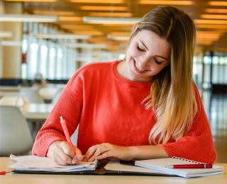 Female student writes in a notebook while studying in a library