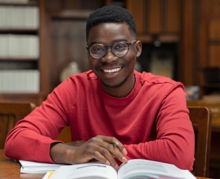 A smiling student in a red sweater studies in a library