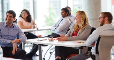 A group of MSBA students sit at tables in a bright room, smiling and engaging in discussion
