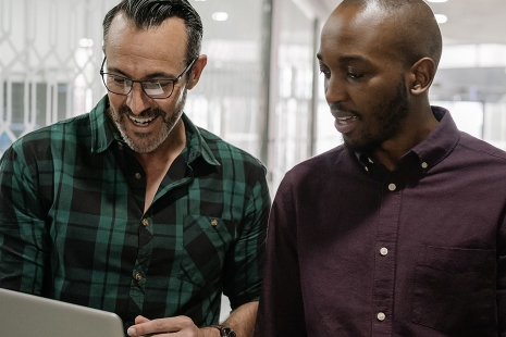 Two men walking in an office and working on a laptop