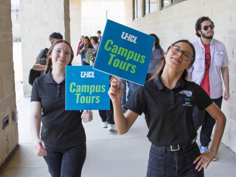 Two student holding UHCL Campus Tours signs