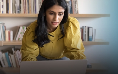 Busy professional woman standing at workplace table, leaning over laptop