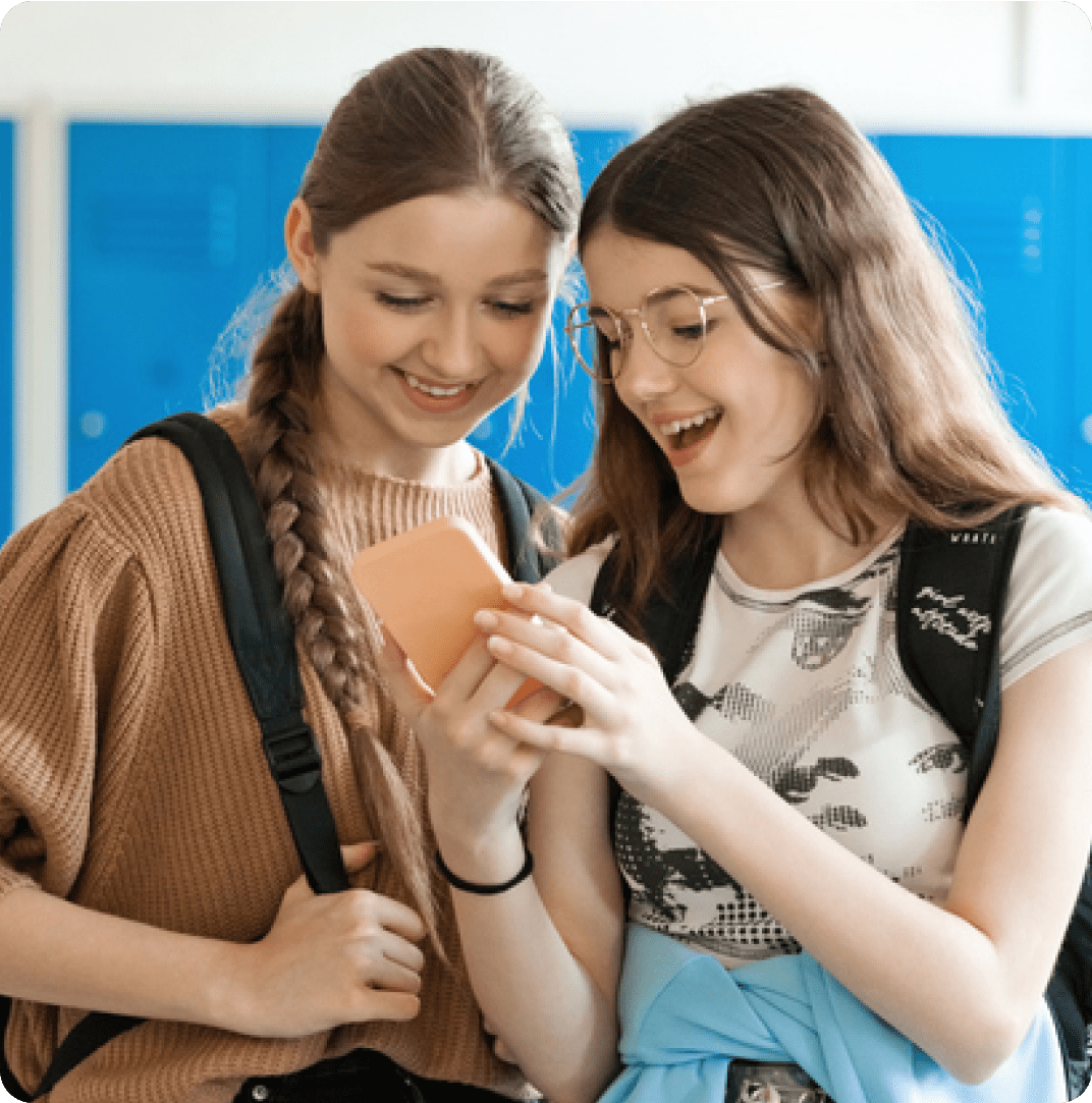 Two young girls smiling at a mobile device.