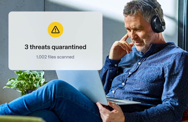 Man using headphones and laptop. Aura app overlay shows 3 threats quarantined with 1,002 files scanned.