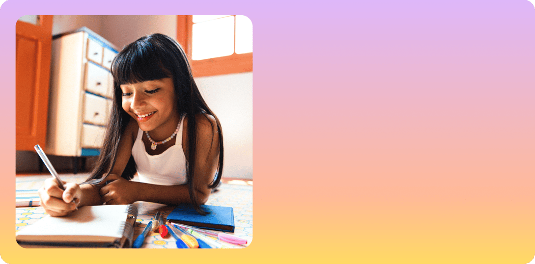 A smiling young girl with long dark hair writes in a notebook while lying on the floor, surrounded by colorful pens and school supplies, against a warm, sunlit background.
