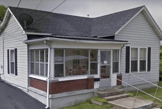 Older home with a detached carport and worn exterior, suitable for renovation or cash sale.