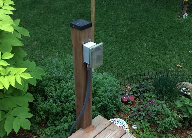 Professional outdoor electrical outlet installation with a weatherproof in-use cover for garden power.