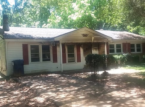 Older home with a detached carport and worn exterior, suitable for renovation or cash sale.