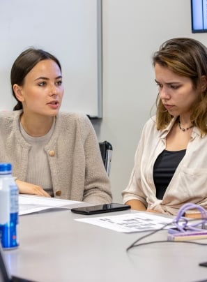 Two female CSUSB students discuss studies at a table.