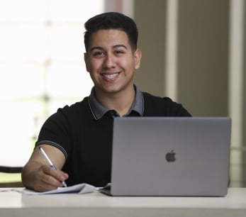 A male CSUSB smiling while working on laptop.