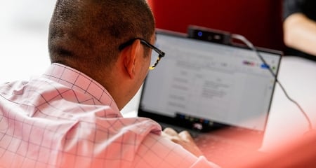 A person wearing glasses works on a laptop, focusing on the screen.