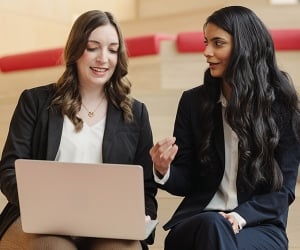 Two Carnegie Mellon MBA students talking while one works on her laptop