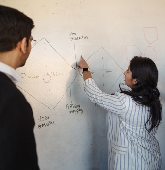 A MSPM points to a diagram on a whiteboard, explaining it to another student