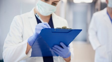 medical professional in mask writing notes on a clipboard