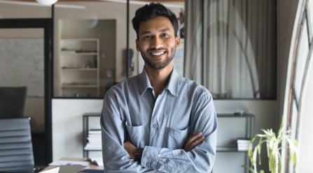 smiling man standing next to office desk with arms crossed
