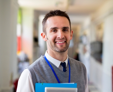 A close-up of a smiling male teacher in a school hallway.