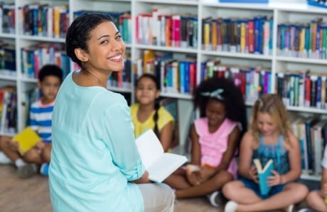 A female teacher smiles while reading to students.