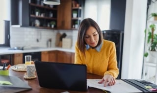 A female reviewing paperwork on table with laptop.