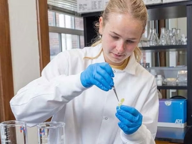 A female bioengineer drops liquid into a sample vial.