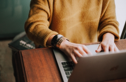 a woman in a yellow jumper and braclet bangles typing on a laptop