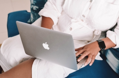a black person in a white outfit and wearing a black apple watch using a laptop on their lap