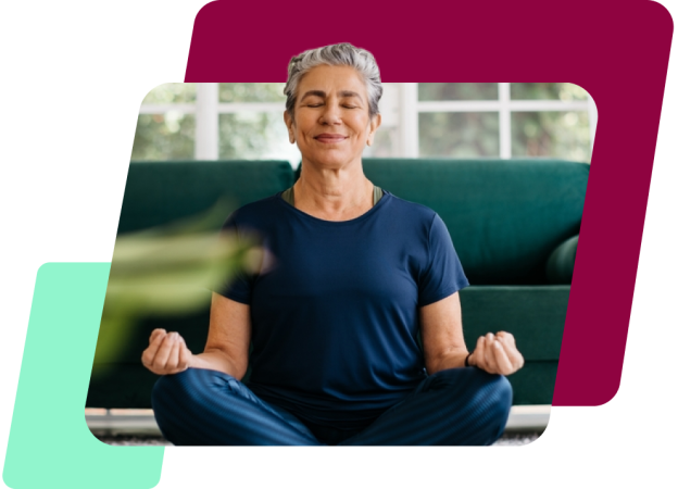 Uma imagem de uma mulher branca de cabelo curto grisalho, meditando de olhos fechados sentada no chão de uma sala, de blusa azul e calça legging também azul.