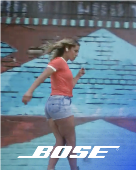 A white Bose logo and a woman wearing bose earphones rollerskating in front of a mural outside.