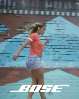 Bose Logo and a women in jean shorts and an orange tshirt rollerskating to music.