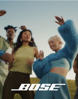 People dancing in a field with a Bose Speaker. A white Bose logo on top of the image. 