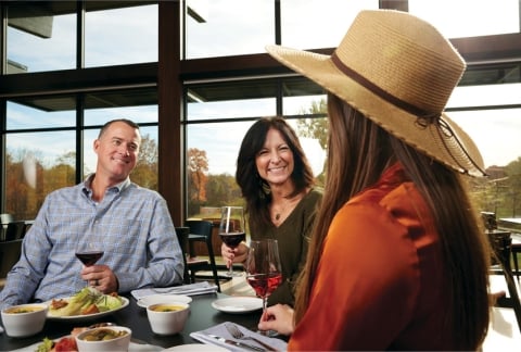 Three adults sitting at table with glasses of wine