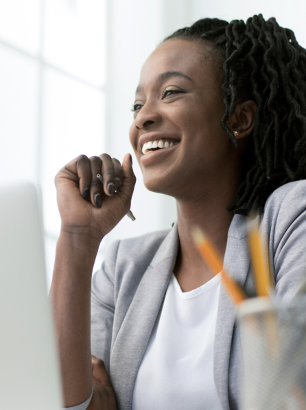 woman sitting at a desk, holding a pen and smiling