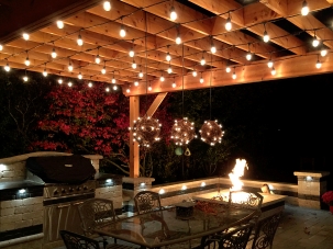 pergola over paver patio with lights, firepit, grill and dining table