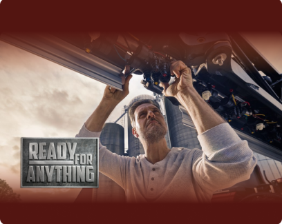 A man sits on the ground near a piece of machinery changing a tiller blade. He wears a blue and white baseball hat and blue shirt. 