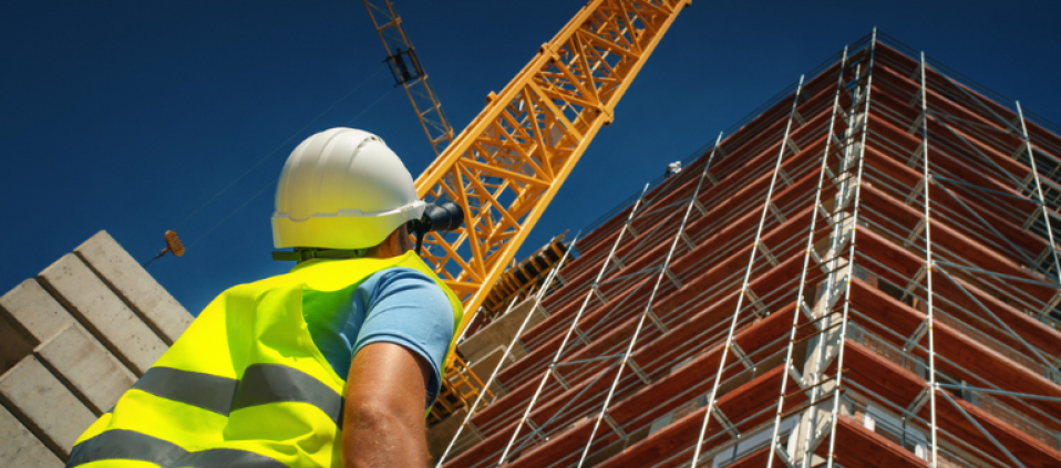 Construction engineer looking up at building with binoculars