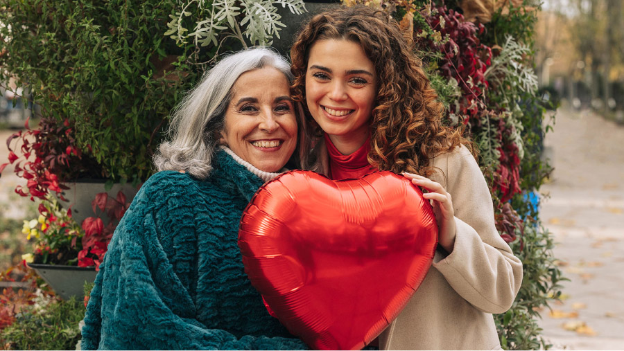 Two Women Smiling While Holding a Heart Shaped Balloon
