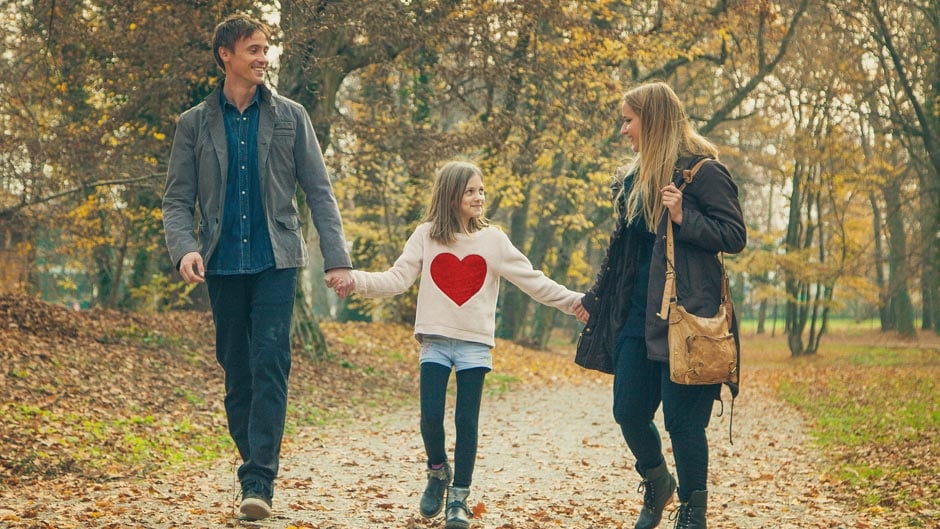 Family walking in fall leaves down a path holding hands