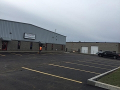 An industrial building with a parking lot and a person walking in the distance.