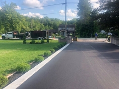Freshly paved driveway with landscapers working in the background.