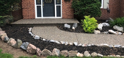 A front entrance of a house with a black door, brick exterior, and a landscaped garden.