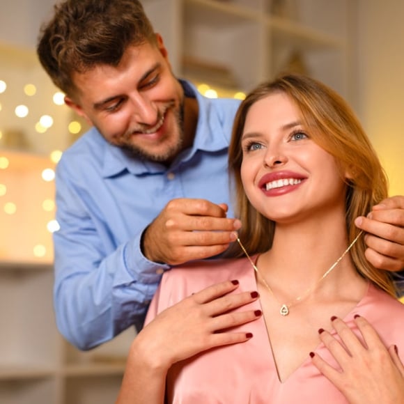 A man assists a woman in fastening a necklace around her neck.