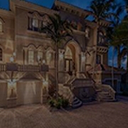 Image of large bricked home at night with lights on and palm trees