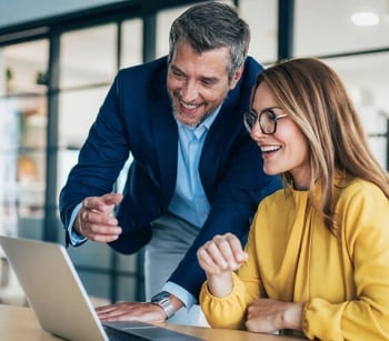 Two coworkers smiling and working together looking at a laptop computer