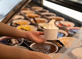 Hand holding a cup of frozen yoghurt with toppings in the background