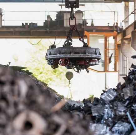 Crane with electromagnet lifting scrap metal in an industrial yard