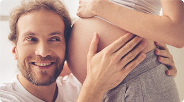 Mann hält Ohr an Bauch seiner schwangeren Partnerin