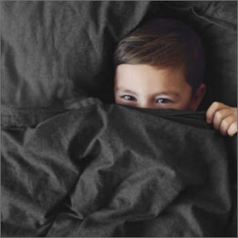 Junge zieht Bettdecke übers Gesicht