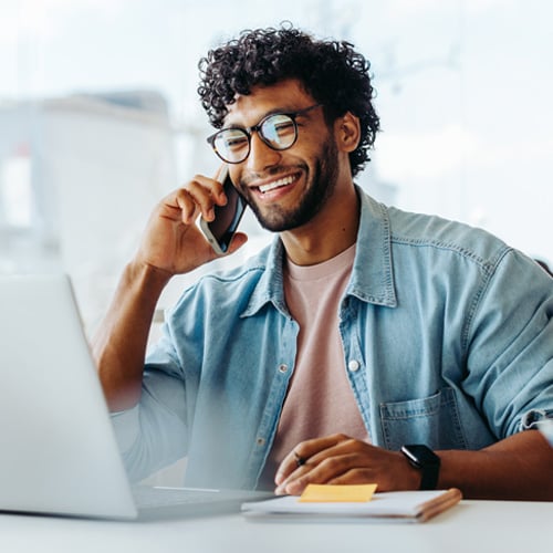 Man smiling while speaking on the phone and looking at laptop
