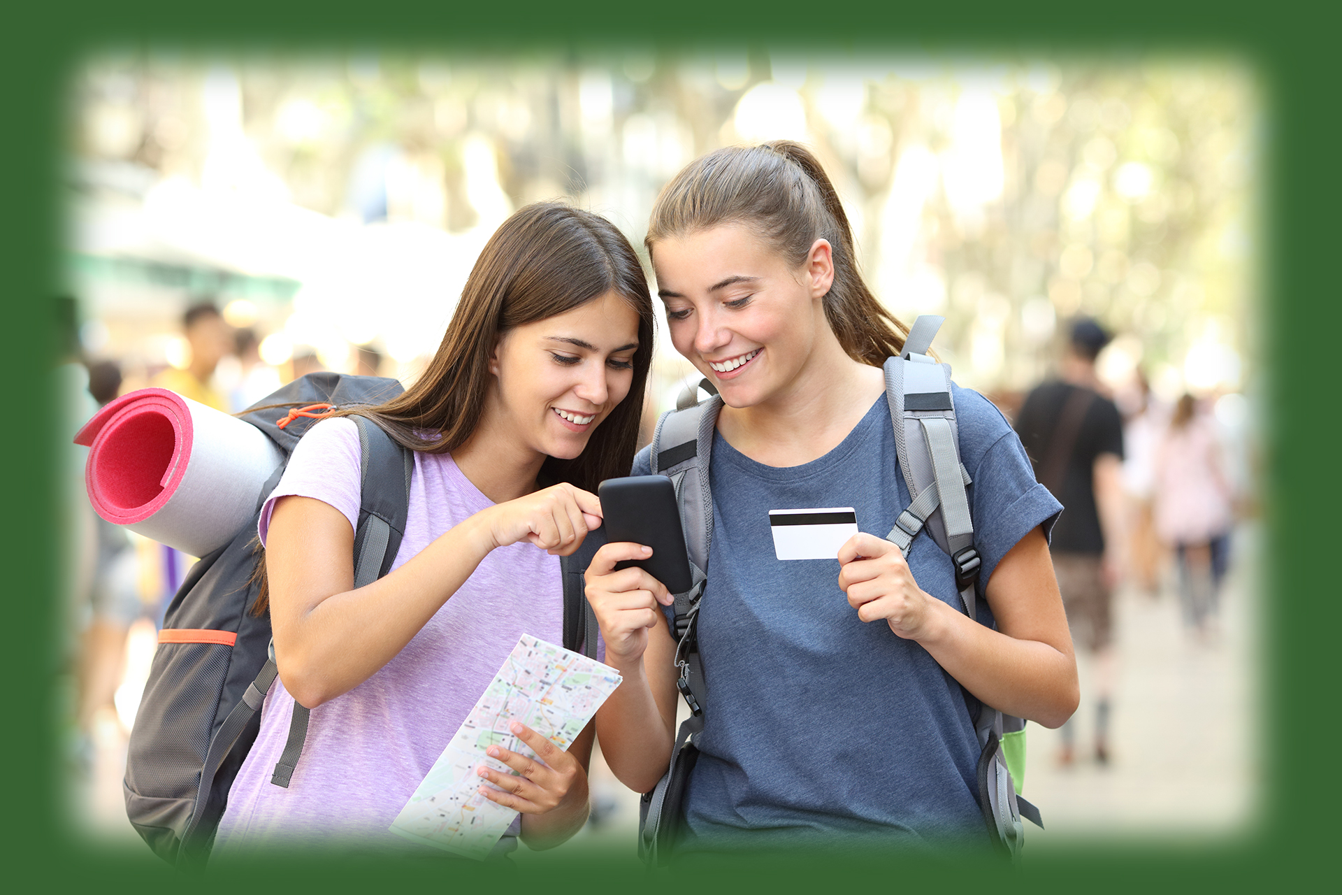 two women smiling and looking at a cell phone, one woman has a debit card in hand