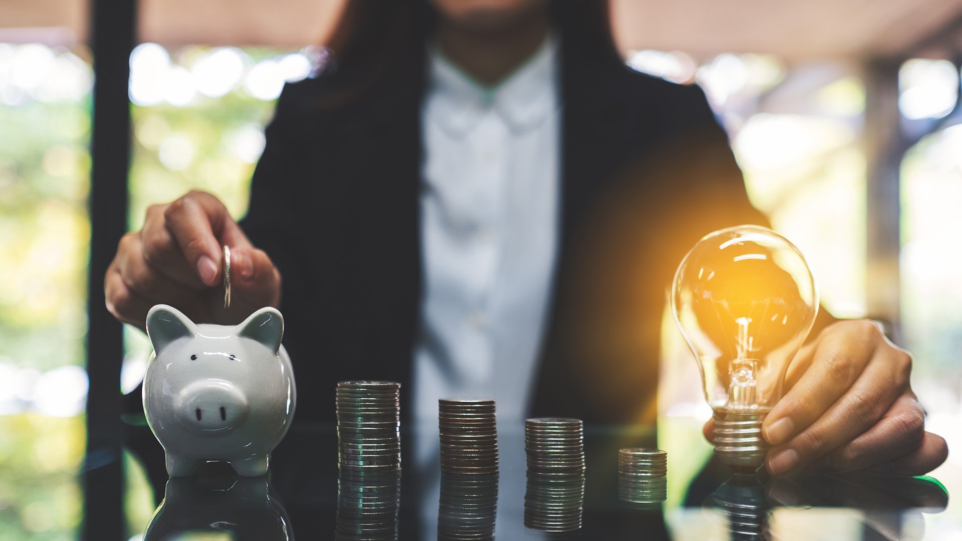 person holding lightbulb and putting coins in piggy bank