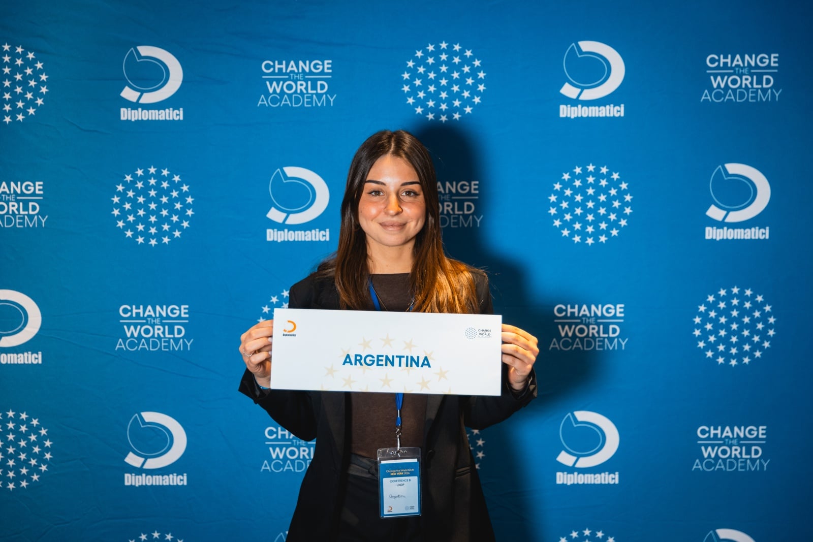 Studentessa con cartellino del proprio paese davanti al backdrop Diplomatici Change the World Academy